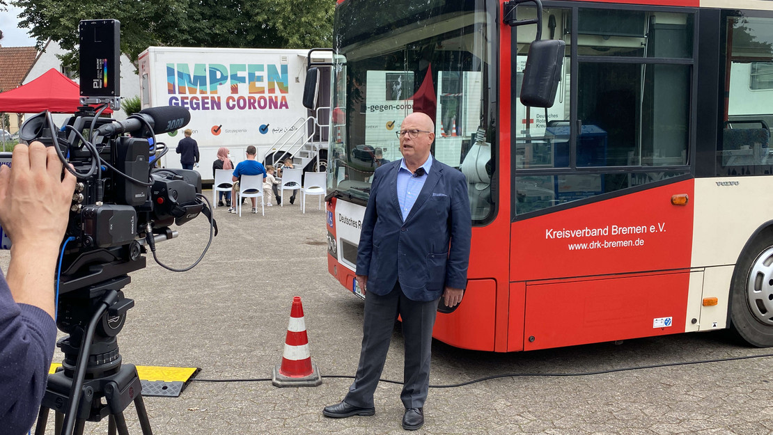 Bremens SoVD-Landesvorsitzender Ein Kameramann nimmt ein Interview mit Joachim Wittrien auf, der vor einem Bus der BSAG steht. Im Hintergrund steht das Impfmobil.
