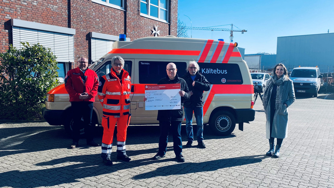 Vor dem Kältebus der Johanniter Obdachlosenhilfe steht eine fünfköpfige Gruppe. In der Mitte ist Joachim Wittrien mit dem Spendenscheck über 1.000 Euro zu sehen.