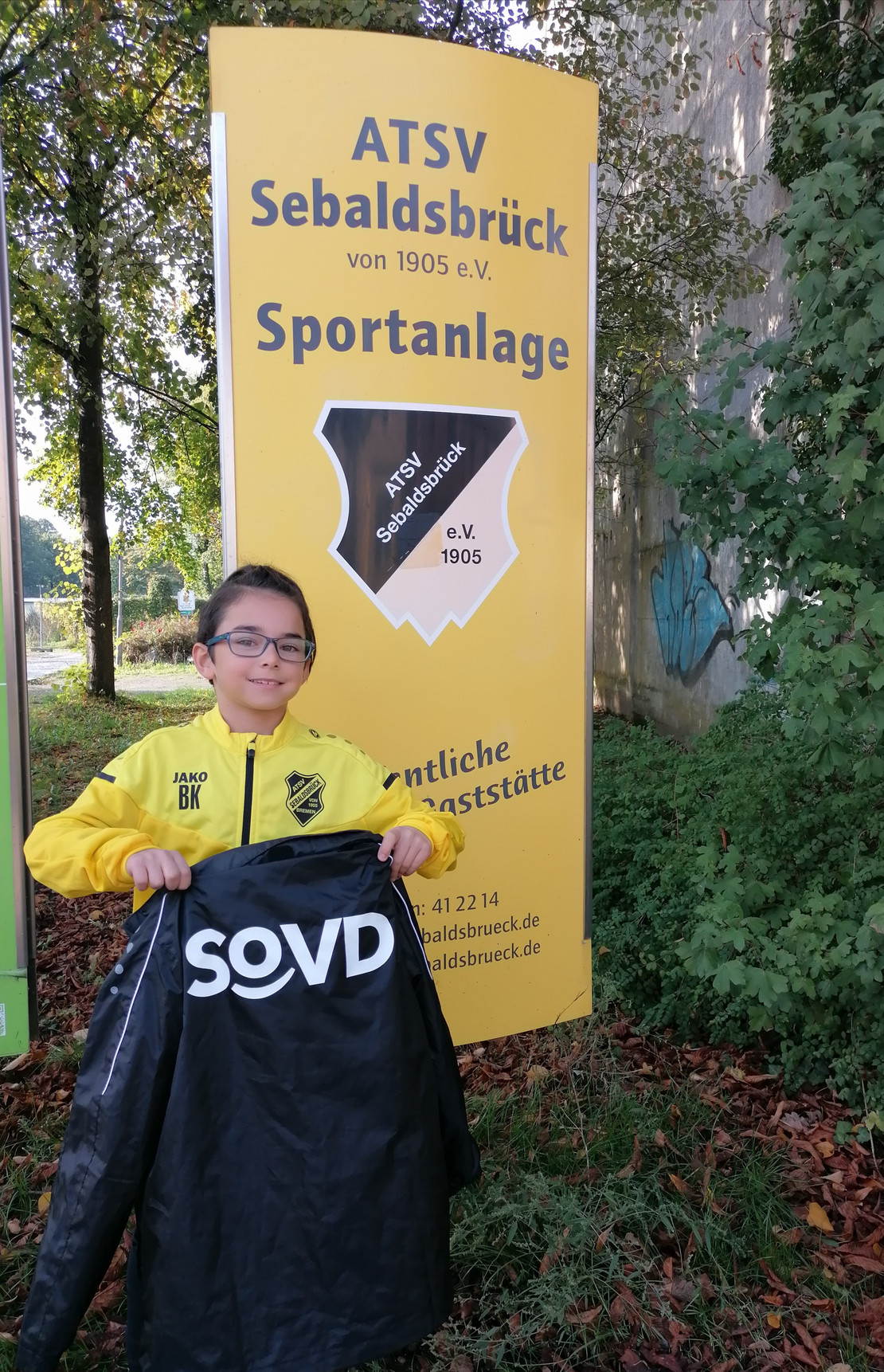 Ein junger Kicker zeigt die schwarze Regenjacke.