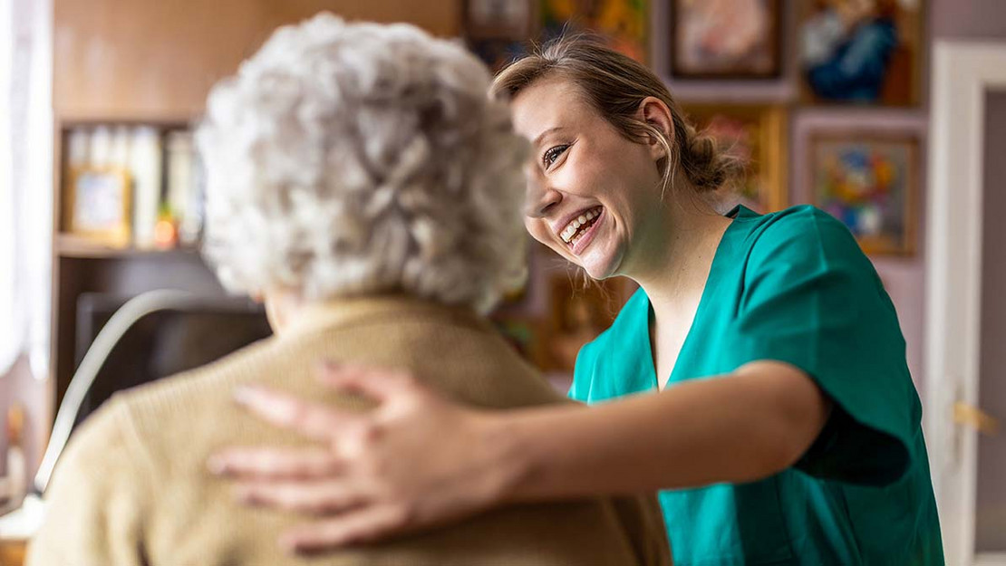 Eine Pflegekraft umarmt eine ältere Frau in einer Wohnung. 