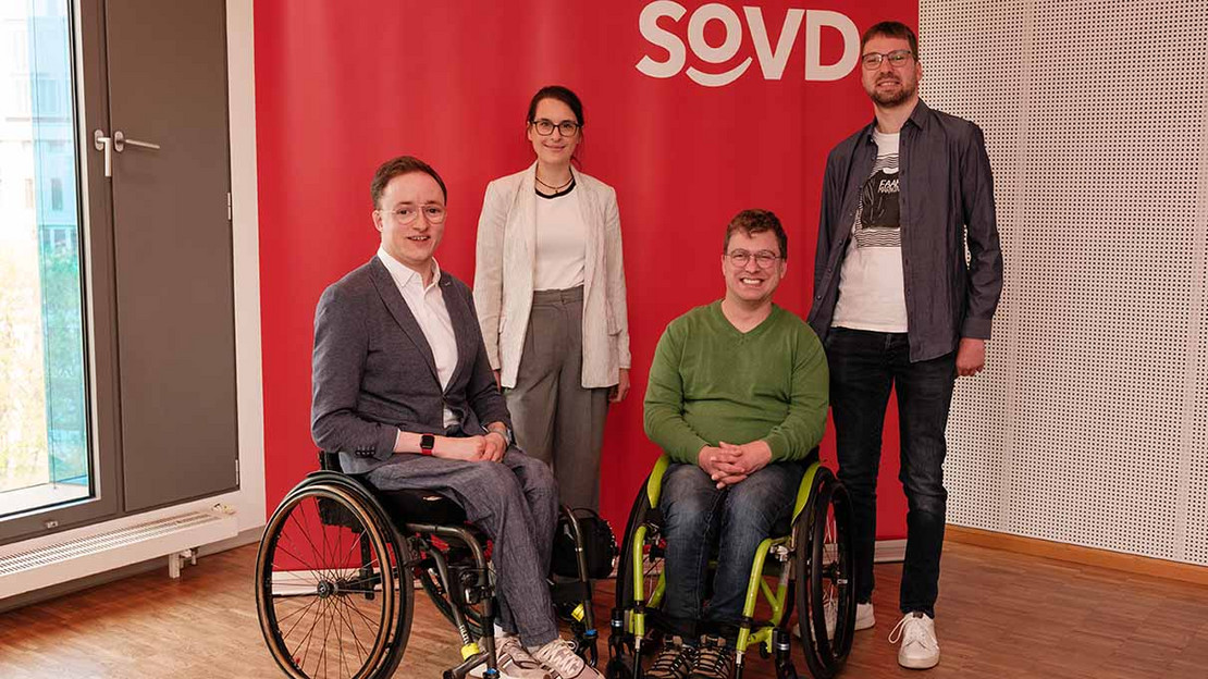 Vier Personen vor einer roten Wand mit dem SoVD-Logo. 