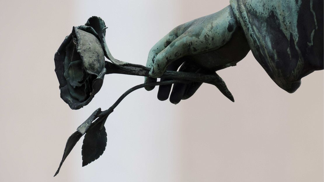 Die Hand einer trauernden Skulptur hält eine Rose