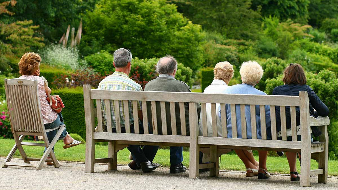 Rückenansicht einer Gruppe älterer Menschen, die in einem Park auf einer Bank sitzt. 