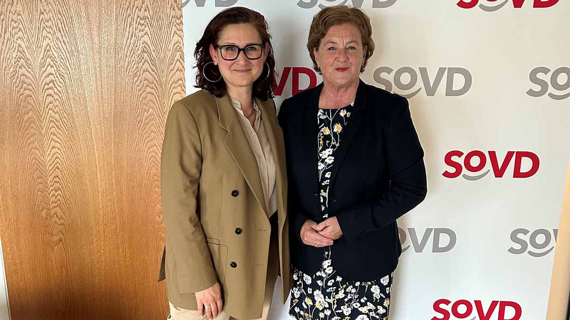 Ferda Ataman und Michaela Engelmeier stehen vor einem Aufsteller mit SoVD-Logos. 
