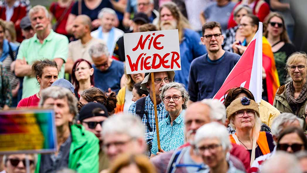 Menschen auf einer Demo gegen Rechts. In der Mitte ein Plakat mit der Aufschrift "Nie wieder". 